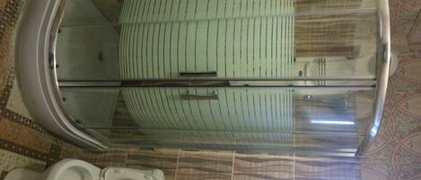 A bathroom with a toilet, a glass shower enclosure, and patterned floor tiles.