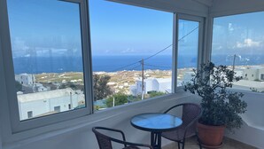 A balcony with a view of the sea and buildings, furnished with wicker chairs and a small table. - Stella Nomikou Apartments (Santorini)