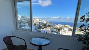 A balcony with two wicker chairs and a small round table, overlooking a coastal town with white buildings and a clear blue sky. - Stella Nomikou Apartments (Santorini)