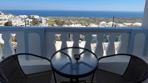 A balcony with two wicker chairs and a glass table, overlooking a coastal town and the sea. - Stella Nomikou Apartments (Santorini)