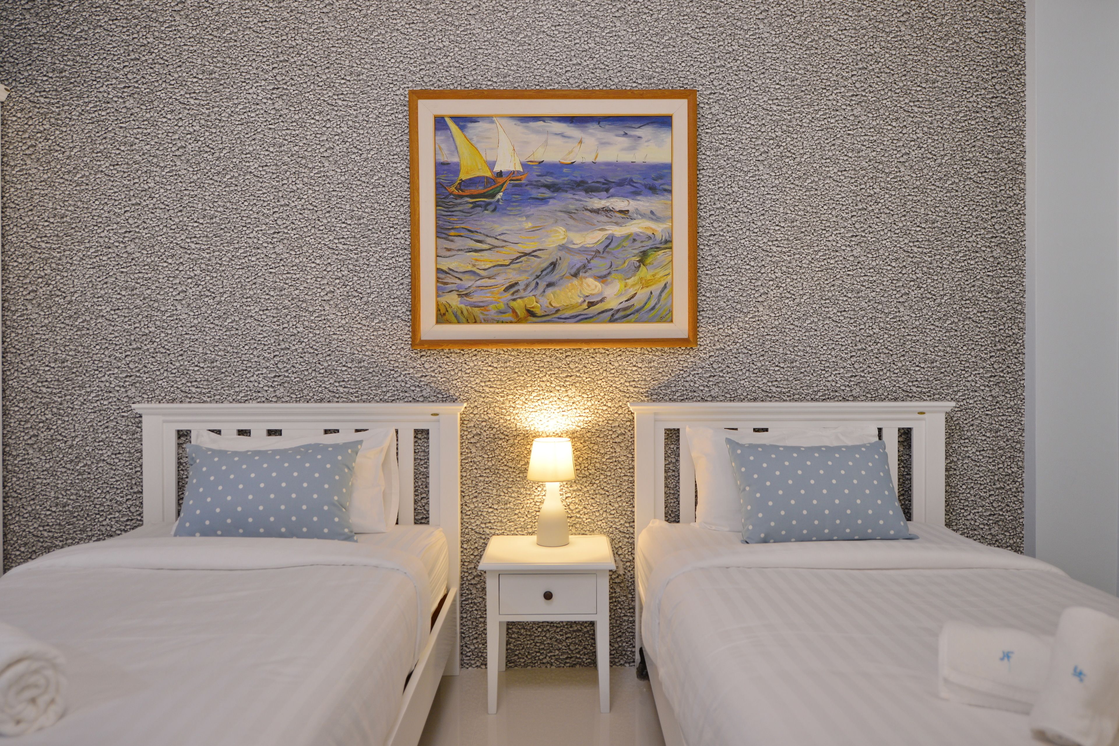 Habitación de hotel con dos camas, un cuadro de un velero en la pared y una mesita de noche con una lámpara.