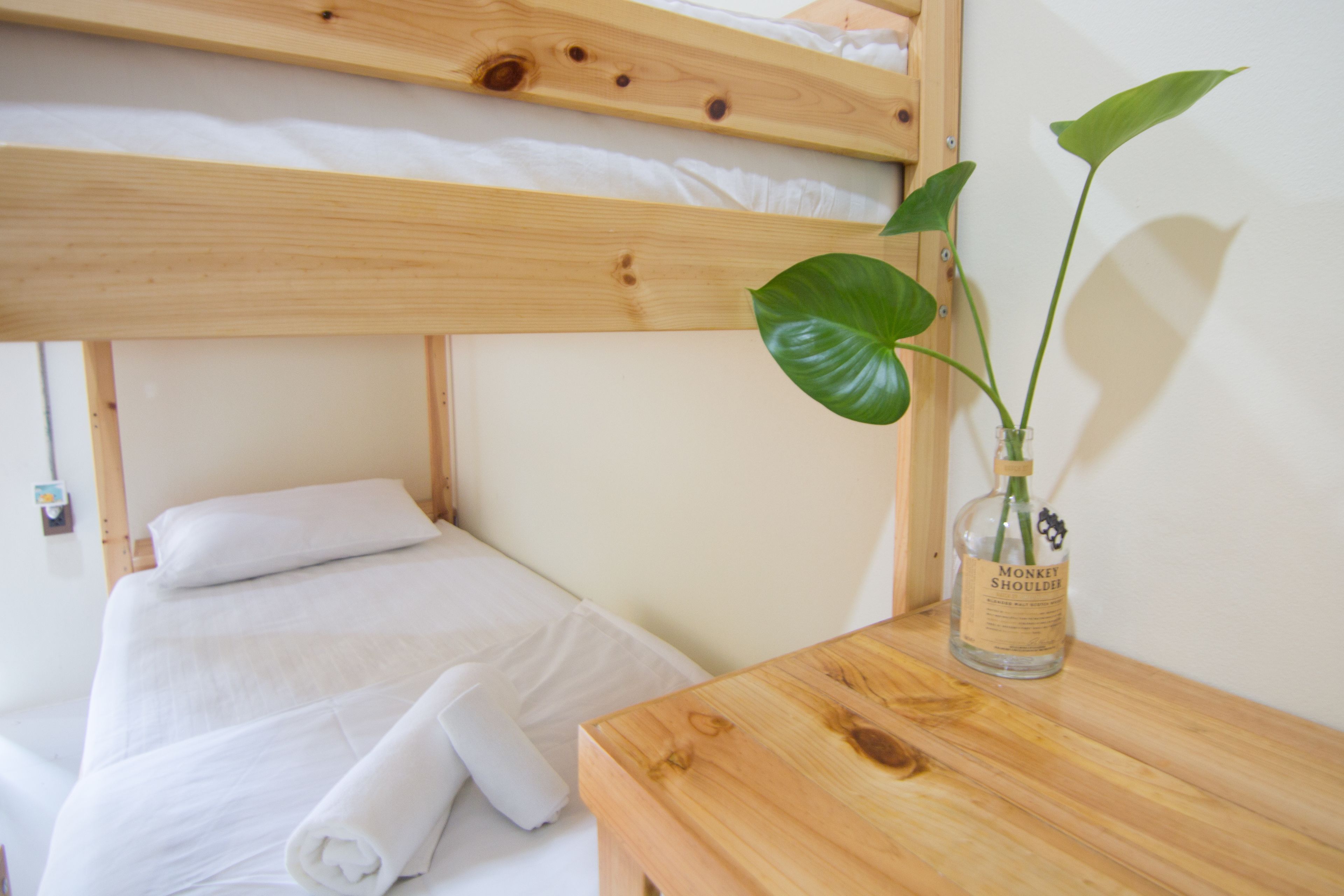 A bunk bed with white bedding and a wooden nightstand with a glass bottle and a plant.