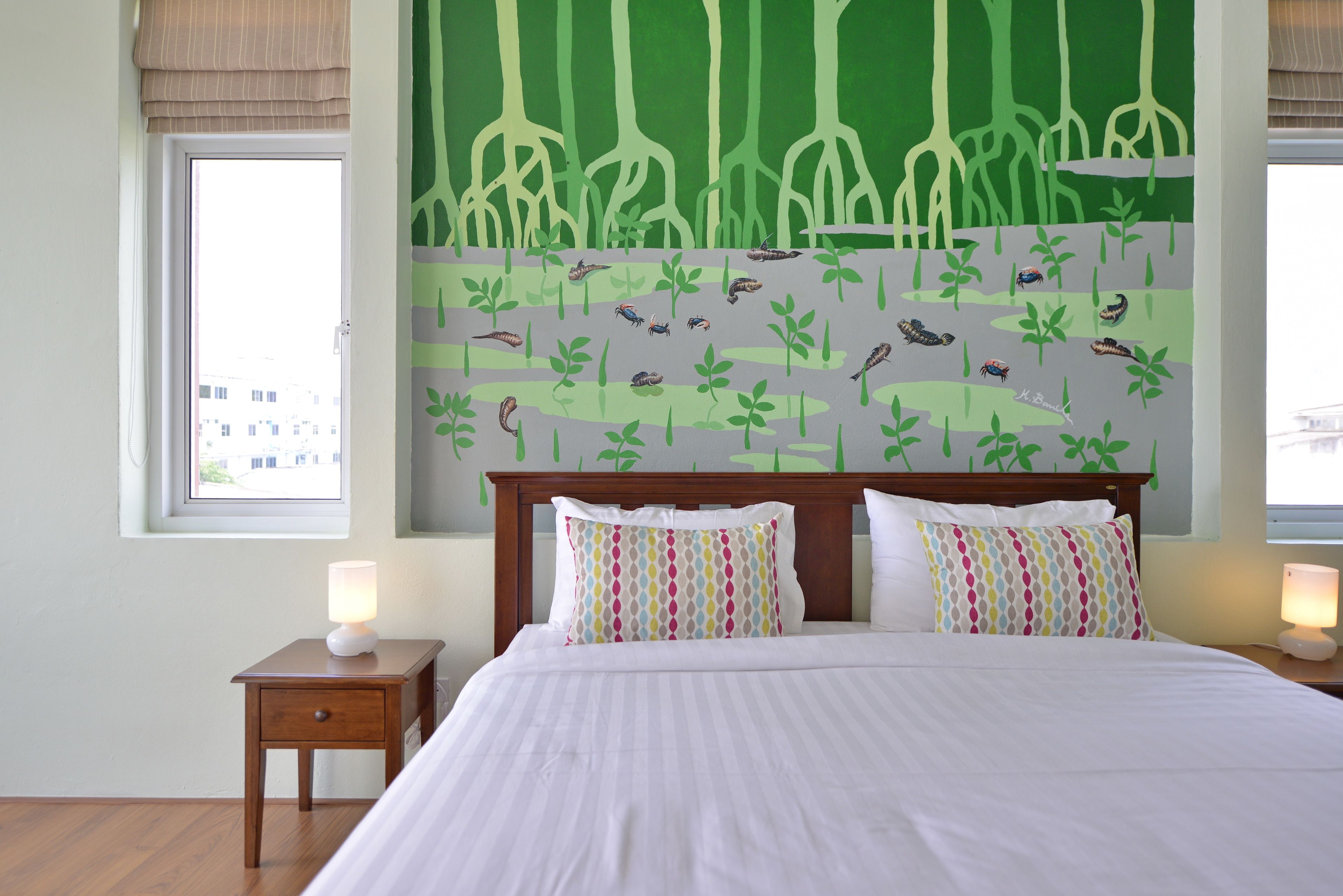 A hotel room with a large bed, two bedside tables, a window, and a mural of a forest scene on the wall.