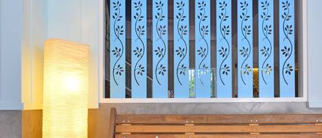 Un banco de madera con cojines a rayas, una lámpara de pie alta y un ventanal decorativo con estampado floral.