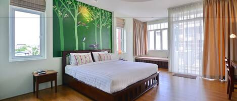 Une chambre spacieuse avec un grand lit, un plancher en bois, un mur décoré d’une fresque verte et de nombreuses fenêtres.