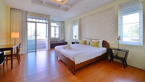A spacious bedroom with a large bed, a desk, and a chair. There is a window with curtains, a ceiling light, and a wall with floral wallpaper. - Just Fine Krabi (Krabi)