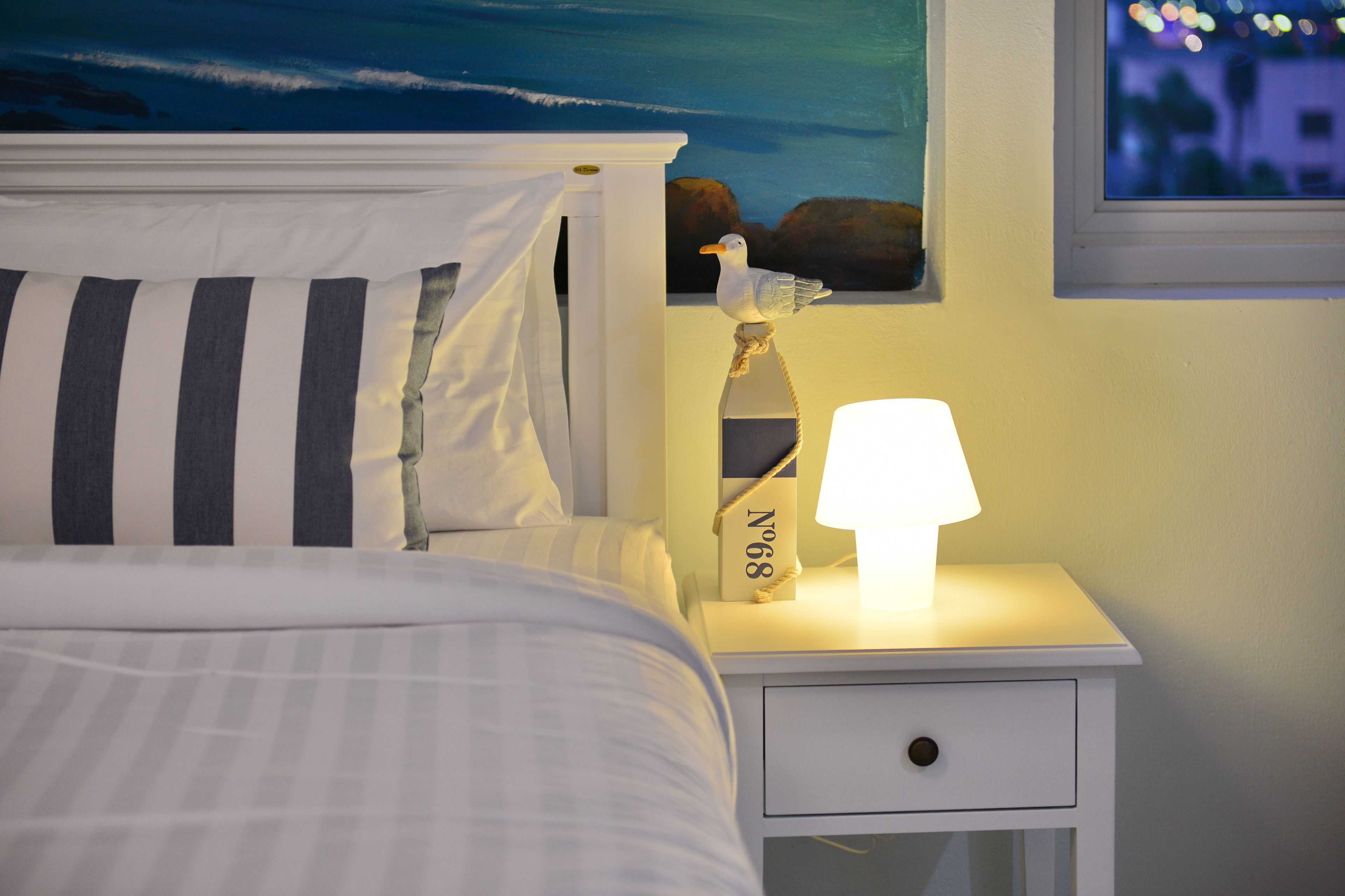 A neatly made bed with striped pillows, a bedside table with a lamp, and a framed picture on the wall.