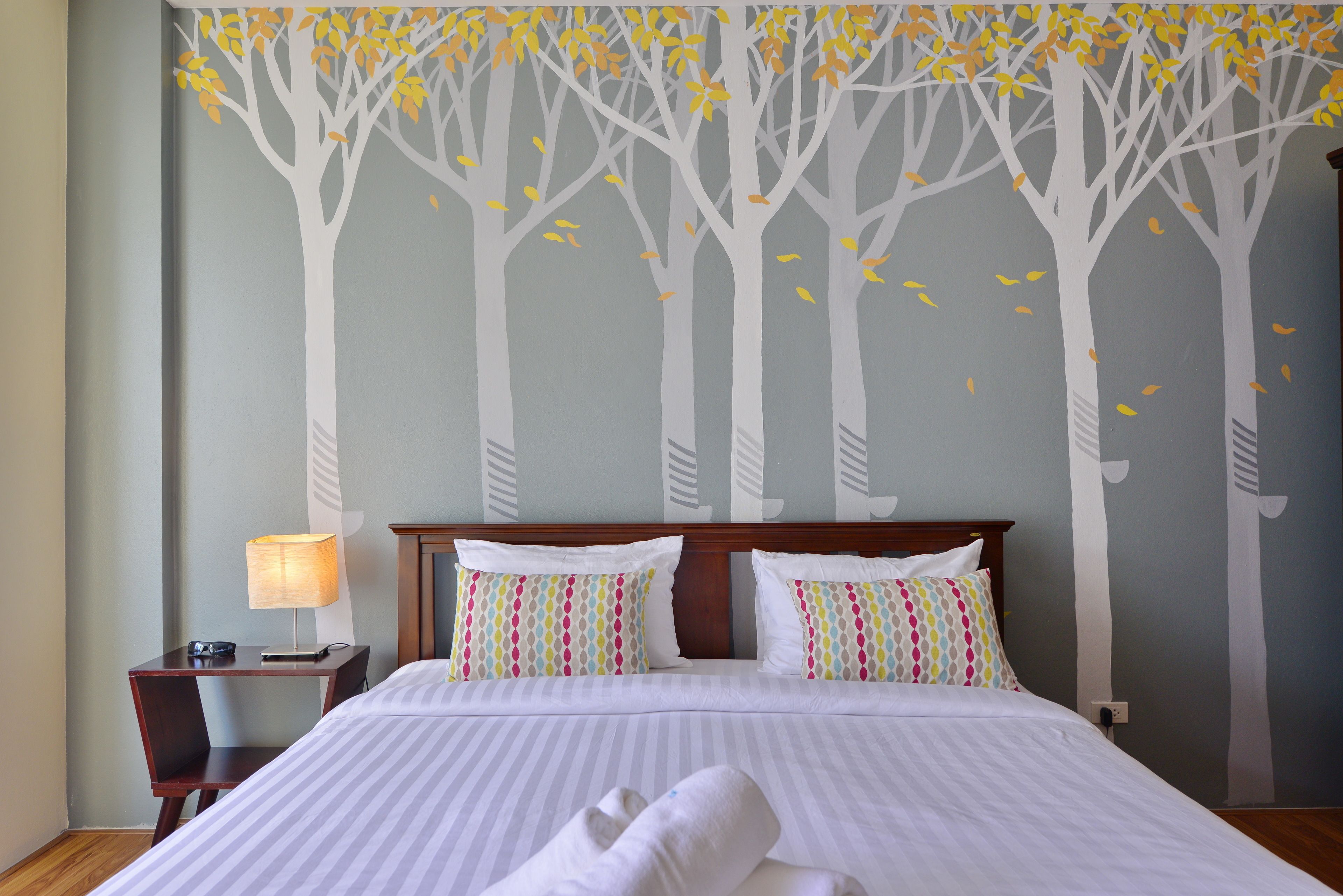 A hotel room with a large bed, two bedside tables, a lamp, and a wall mural of trees.