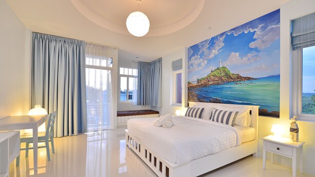 A modern hotel room with a large bed, a desk, and a painting of a coastal scene. - Just Fine Krabi (Krabi)