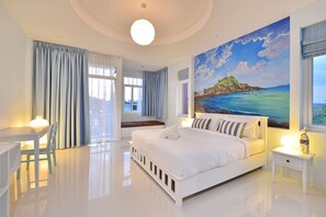 A modern hotel room with a large bed, a desk, and a painting of a coastal scene. - Just Fine Krabi (Krabi)