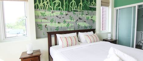 A neatly made bed with white linens and a set of towels, a bedside table with a lamp, and a wall mural of a forest scene.