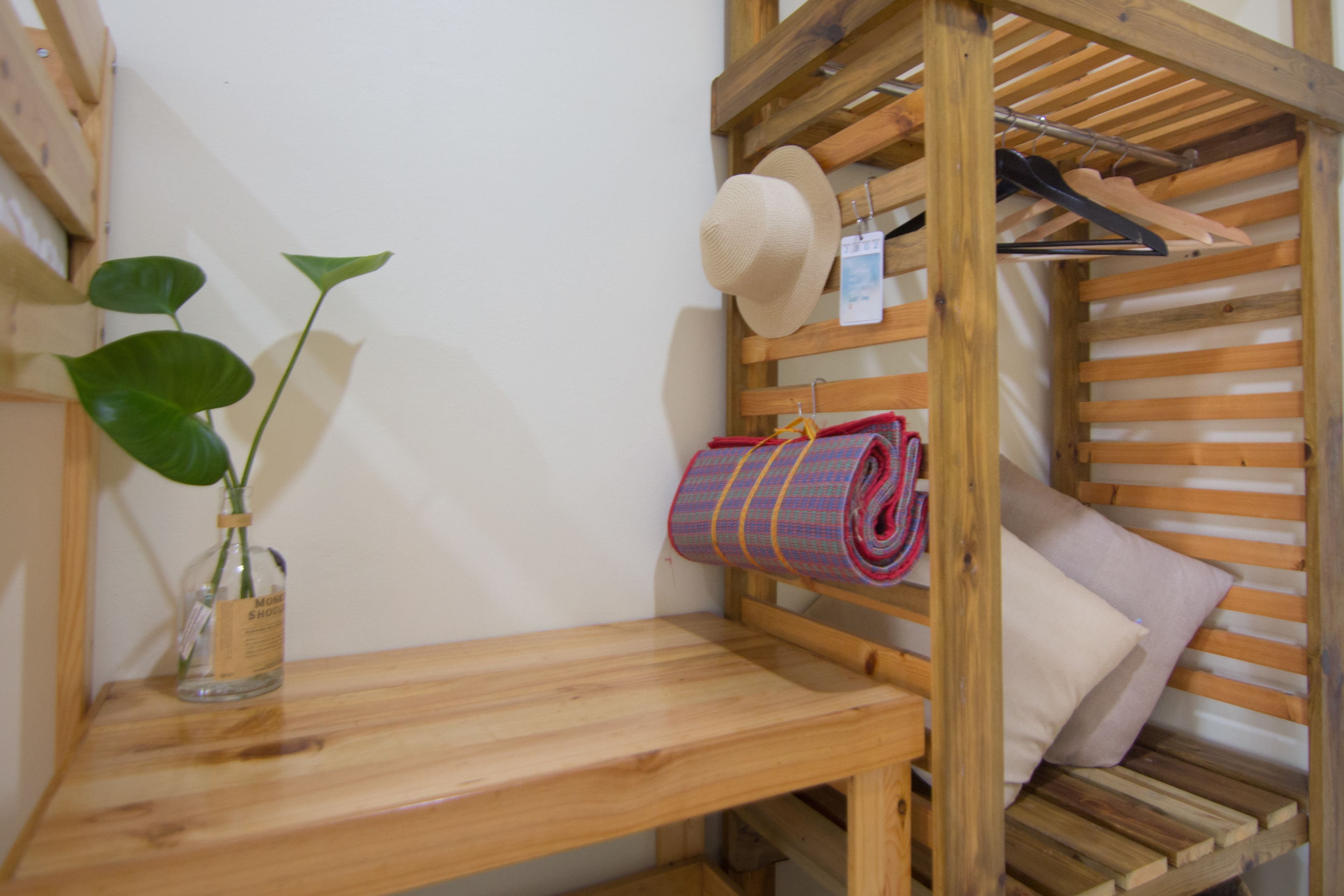 Un lit superposé en bois avec une étagère en dessous, une serviette enroulée, un chapeau et une plante dans un vase en verre.