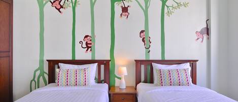 A room with two beds, a nightstand, and a wall with a tree and monkey decal.