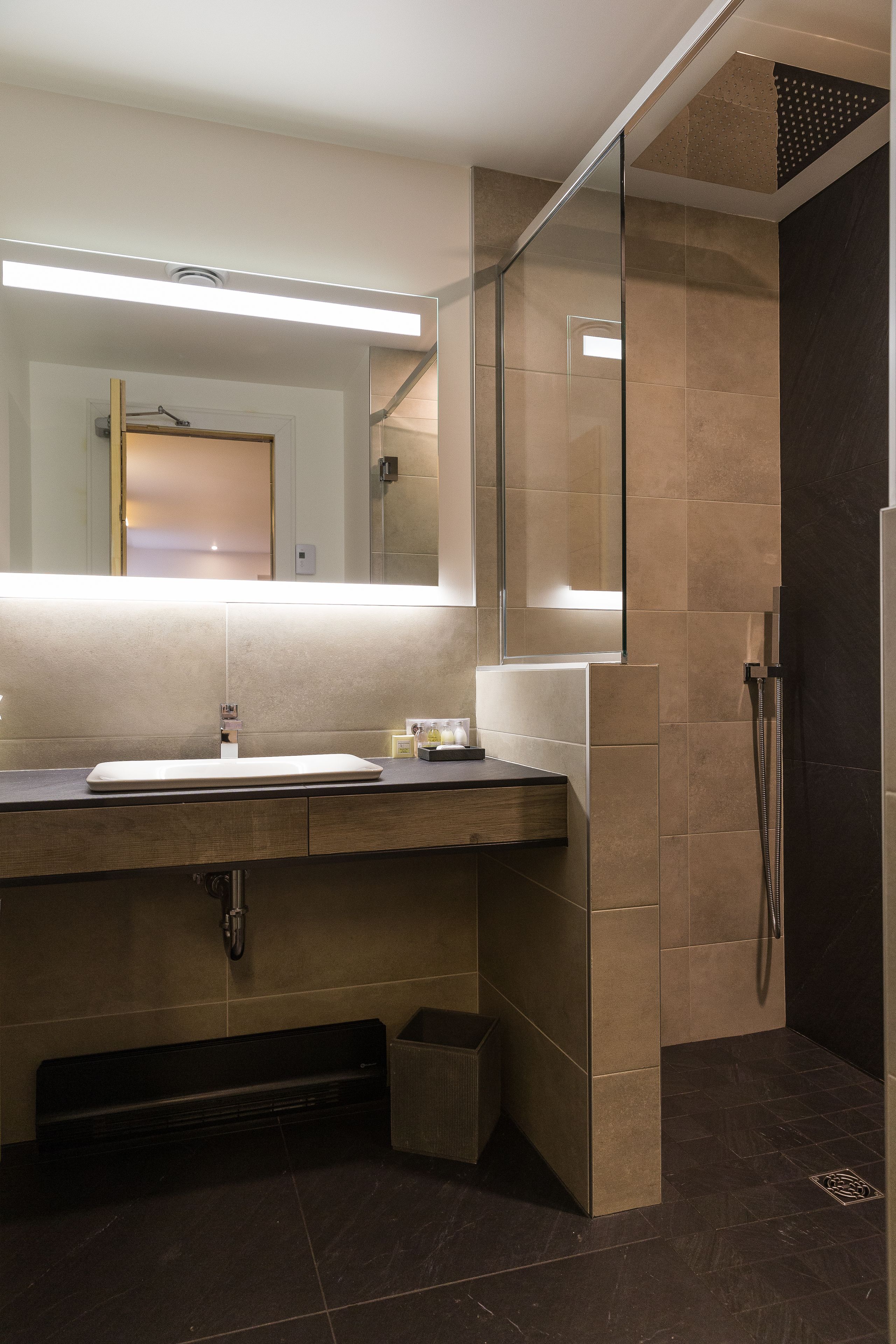 Une salle de bain moderne avec un grand miroir, un lavabo et un espace douche.