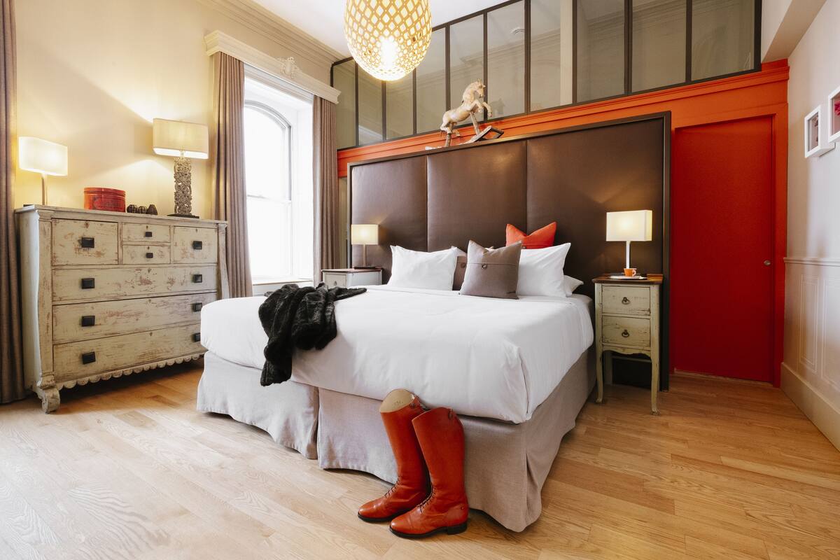 A bedroom with a large bed, a dresser, a nightstand, and a red door.