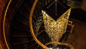 A grand spiral staircase with a golden handrail and a chandelier. - Hôtel Nomad - Vieux Québec (Québec City)