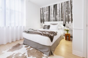 Un dormitorio con cama, alfombra de cuero de vaca, mesita de noche con un florero y un tapiz mural con temática forestal.