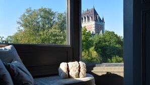 A view from a window with a bench and pillows, overlooking a large building with a tower. - Hôtel Nomad - Vieux Québec (Québec City)