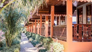 A corridor with wooden columns and balconies, surrounded by lush greenery.