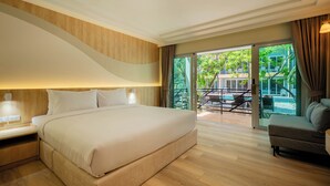A modern hotel room with a large bed, a sofa, and a balcony with a view of greenery and a pool.