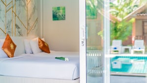 A bedroom with a bed, pillows, and a view of a swimming pool through a glass door.