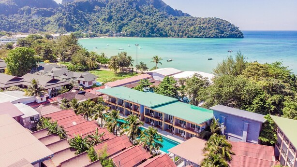 A resort with multiple buildings, a swimming pool, and a view of a turquoise sea and a forested hill.