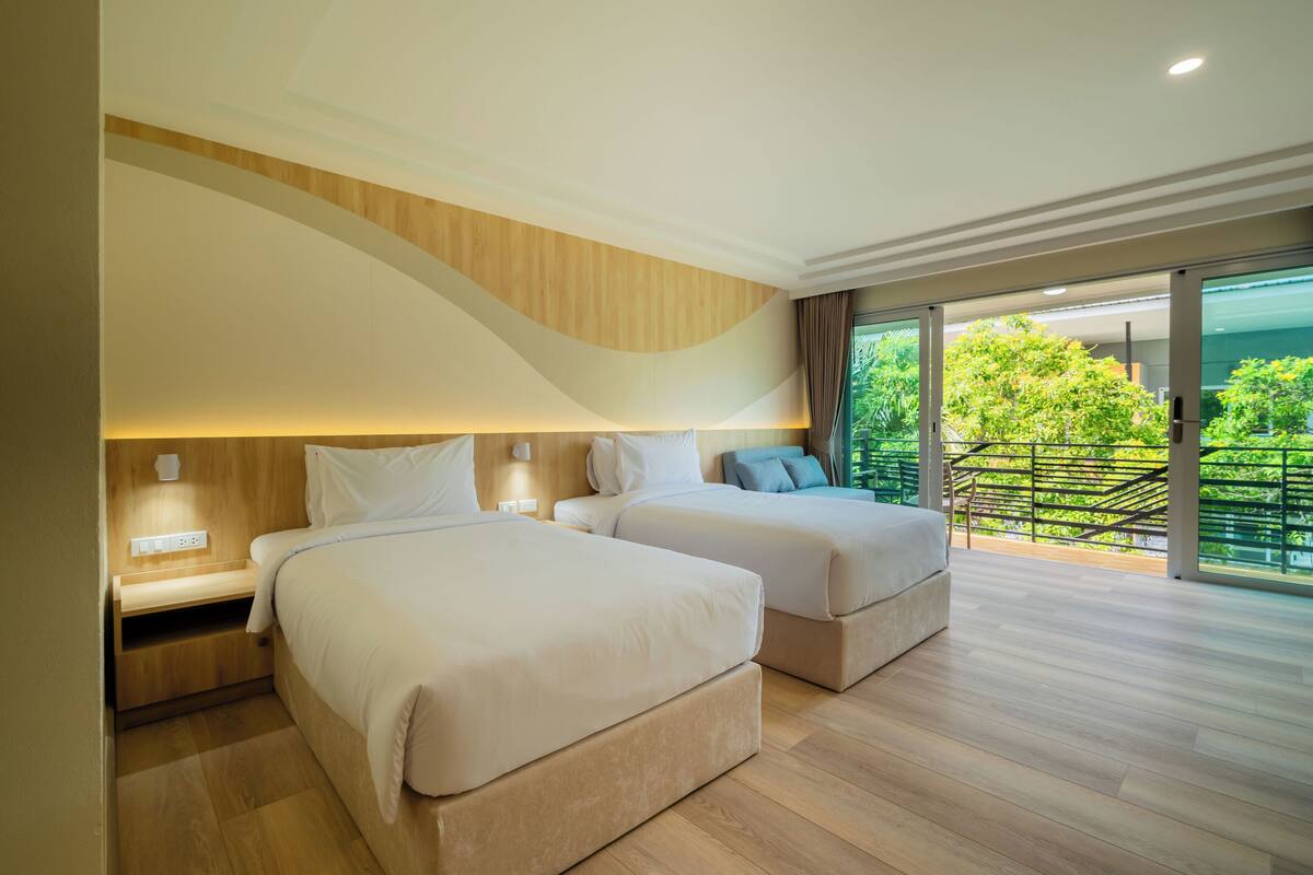 Une chambre d’hôtel moderne avec deux lits, un plafond en bois et un balcon offrant une vue sur la verdure.
