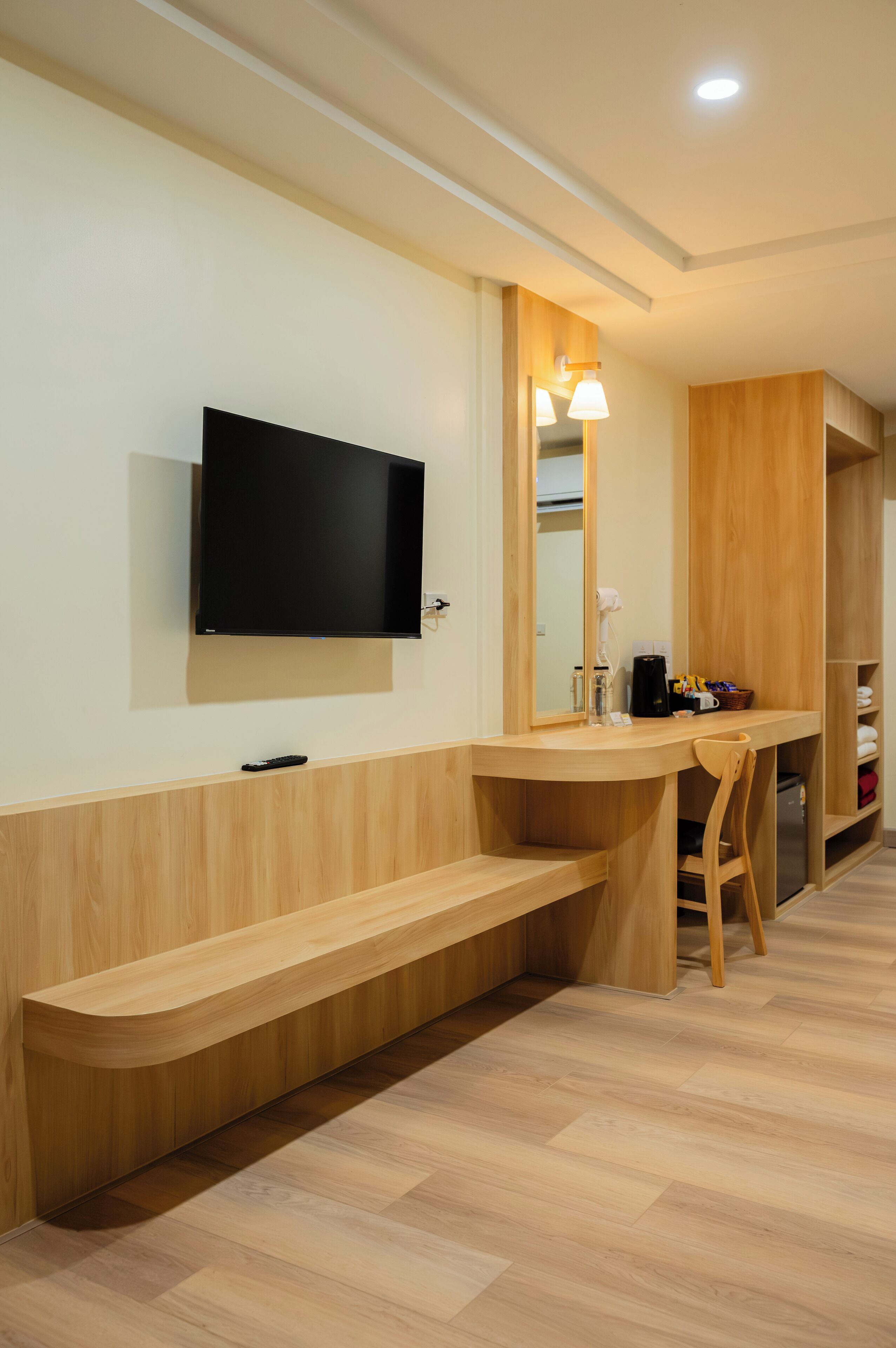 A modern hotel room with a wooden vanity, a mounted TV, and a mirror.