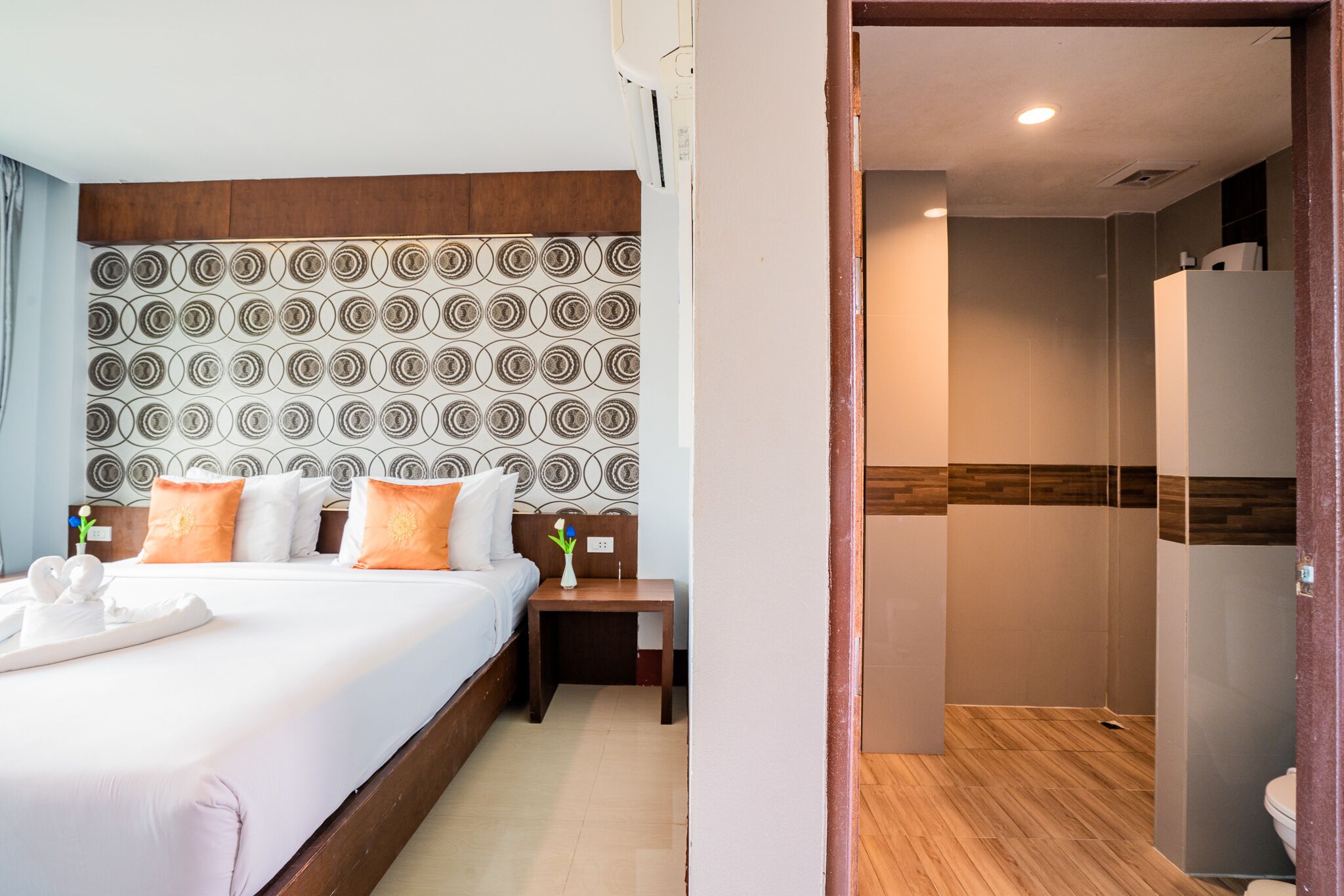 Una habitación de hotel con una cama grande, un cabecero de madera, una mesita de noche y un baño con ducha e inodoro.