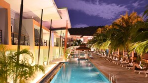 A swimming pool with lounge chairs and palm trees, surrounded by buildings with balconies.