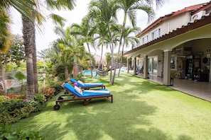 A poolside area with lounge chairs, a hammock, and a building with a tiled roof. - Hibiscus Beach House (Jan Thiel)