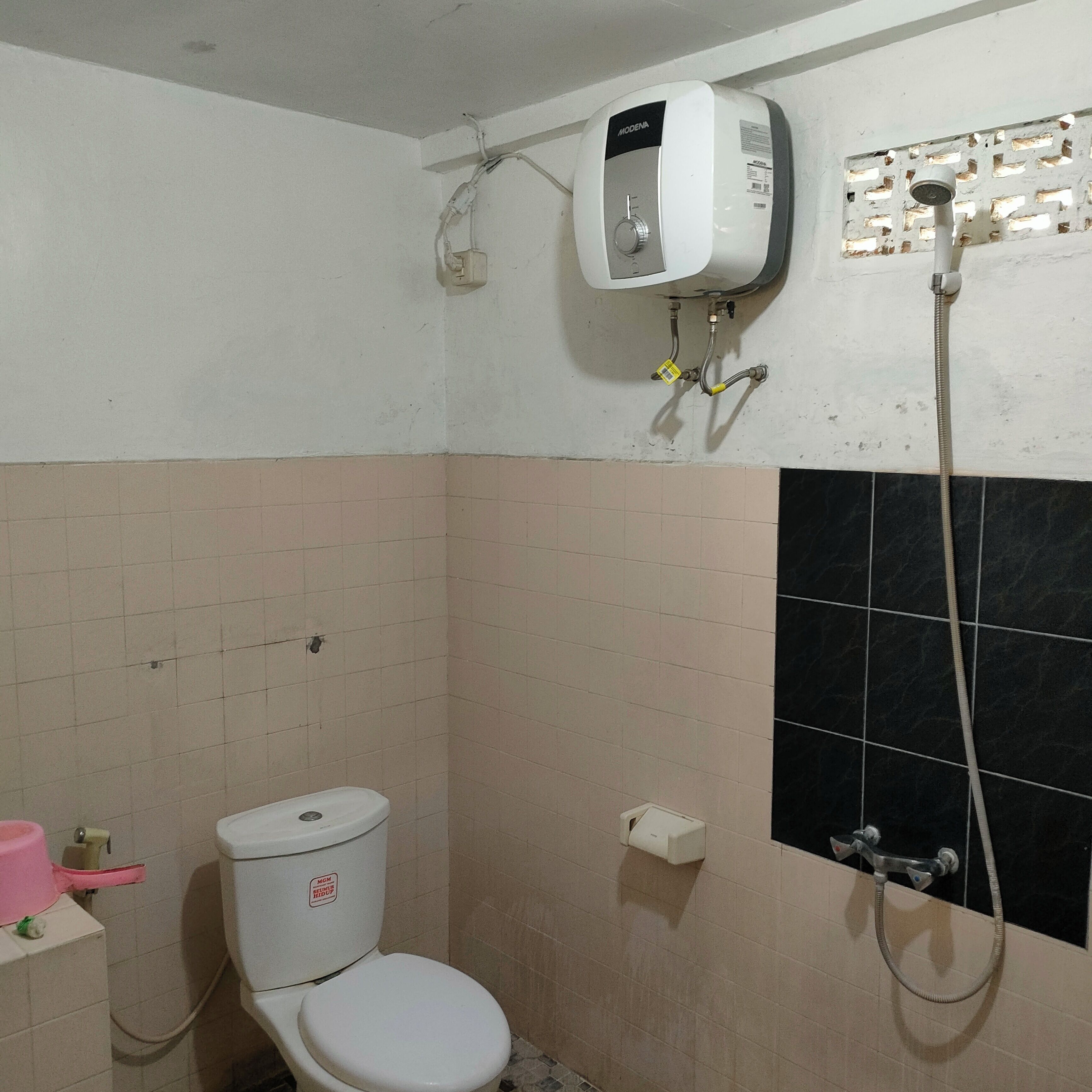 Un baño con inodoro, ducha y calentador de agua instalado en la pared.
