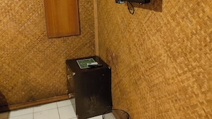 Un baño con un muro tejido, un armario de madera y un armario negro, además de un televisor fijado a la pared.