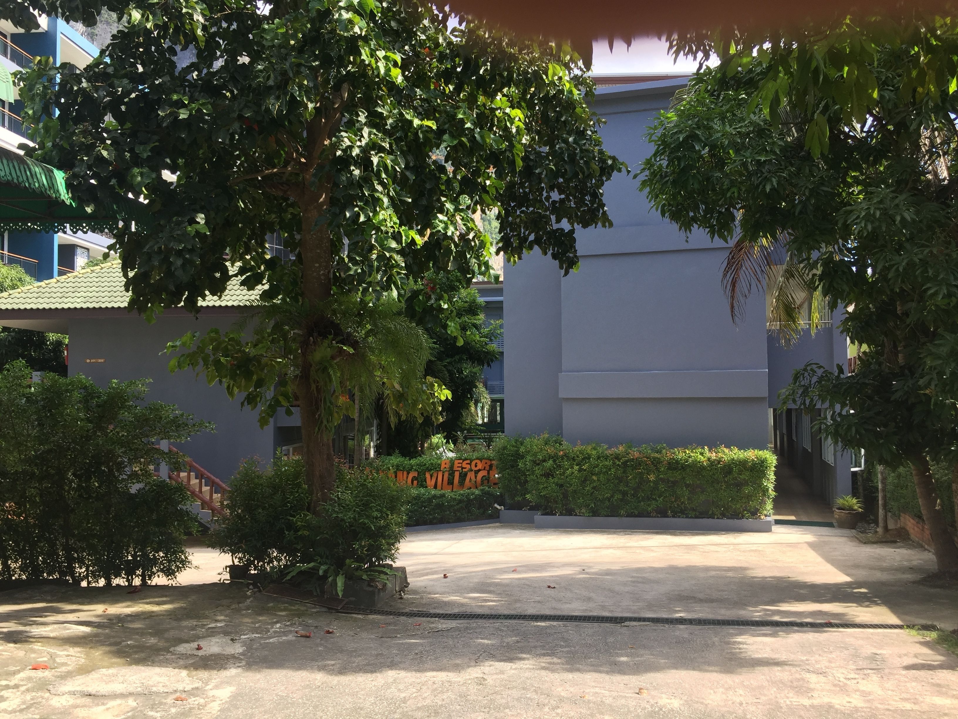 A courtyard with a paved walkway, surrounded by greenery and a building with a grey facade.