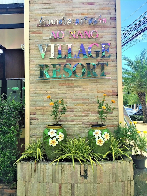 Señal para AO NANG Village Resort, con un fondo de pared de piedra y dos macetas grandes con flores.