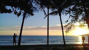 Escena de playa con palmeras y el océano al atardecer.