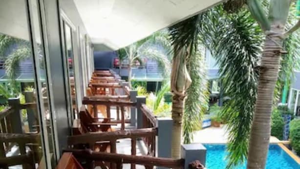Un espacio al aire libre con techo, con mesas y sillas de madera, con vistas a una piscina y palmeras.