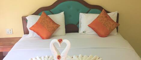 Habitación de hotel con cama, almohadas, una lámpara de pared y un cuadro de una playa.