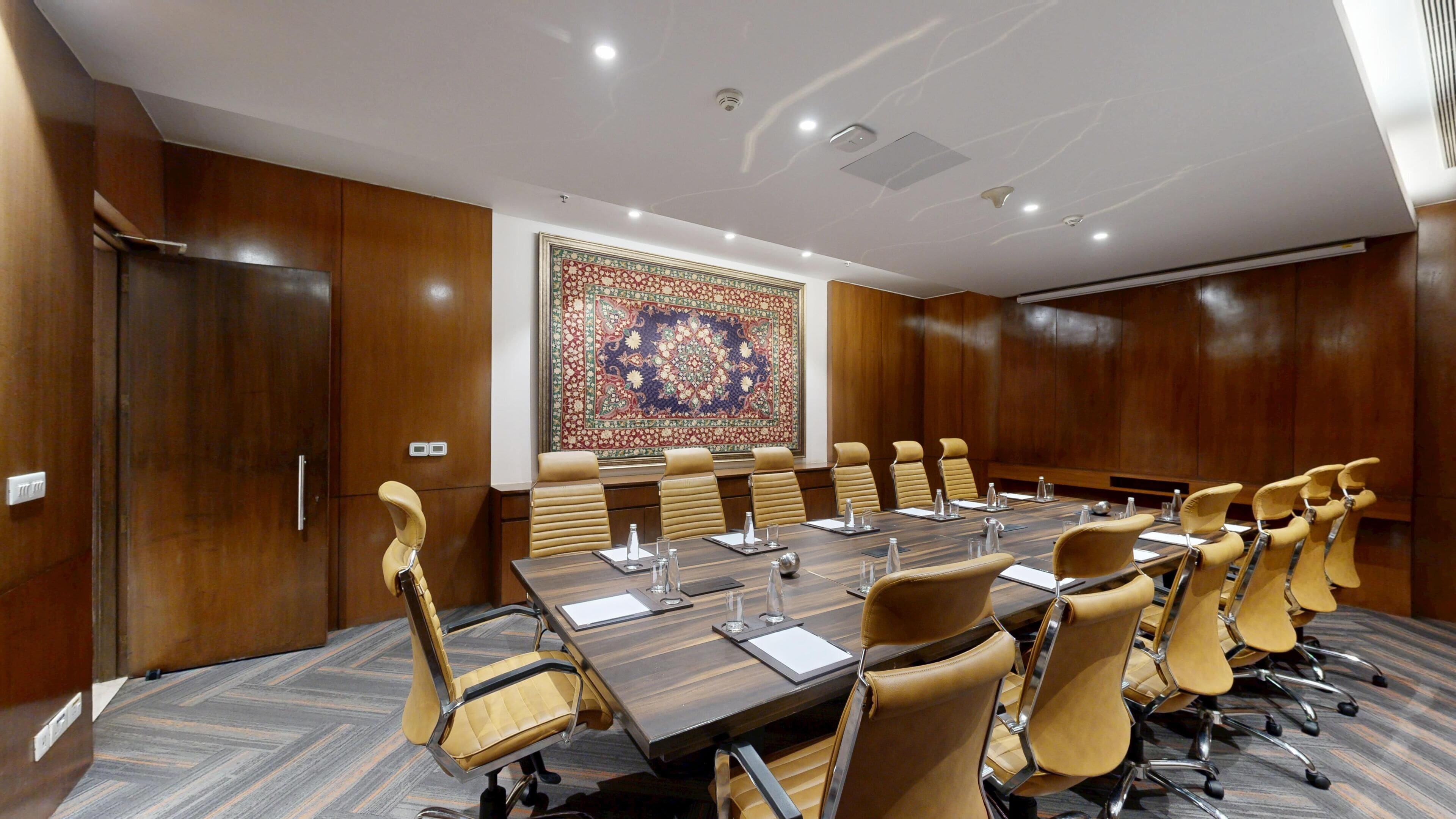 A conference room with a long table, multiple chairs, and a decorative carpet.