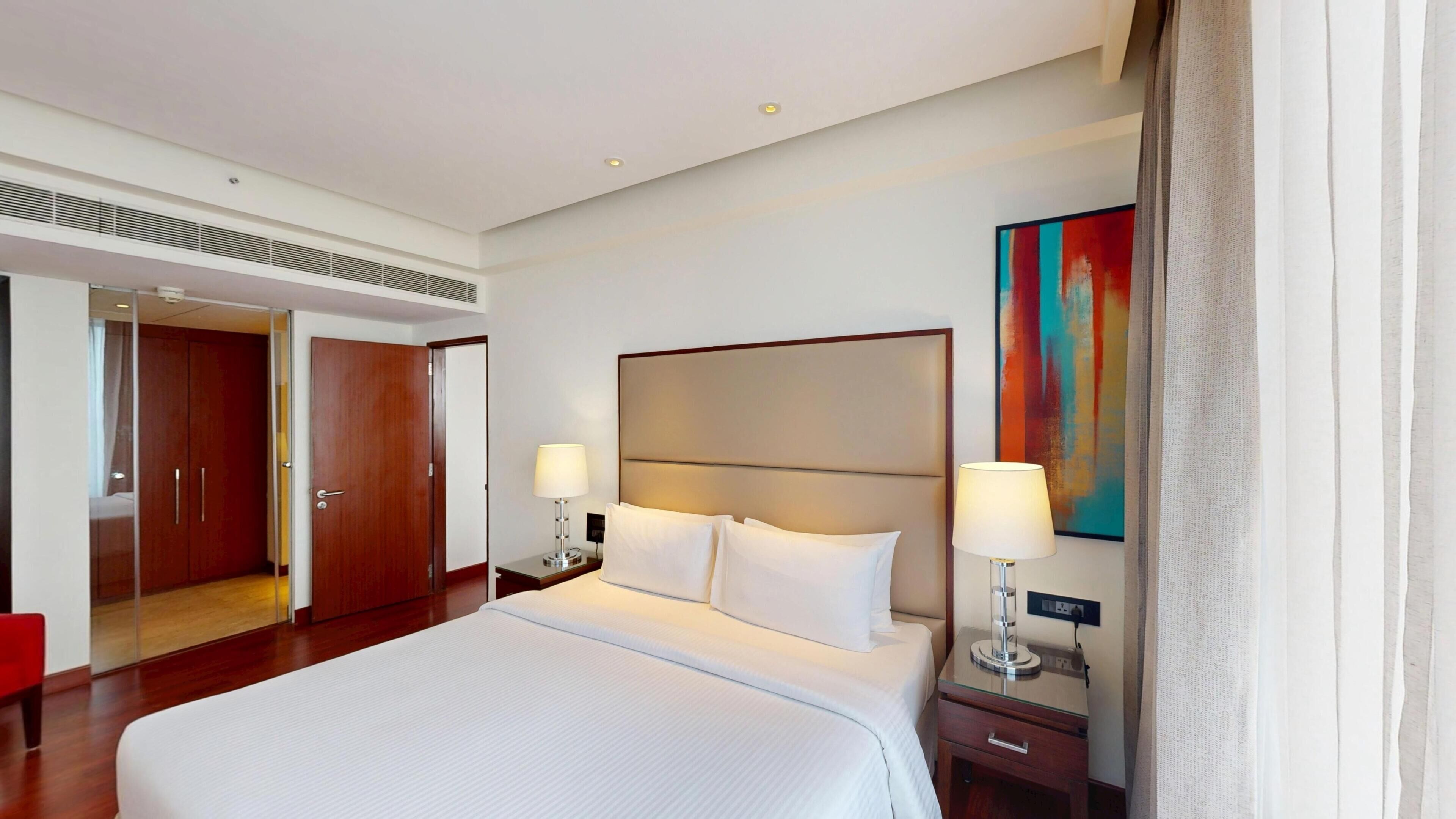 A hotel room with a large bed, two bedside tables, a wardrobe, and a painting on the wall.