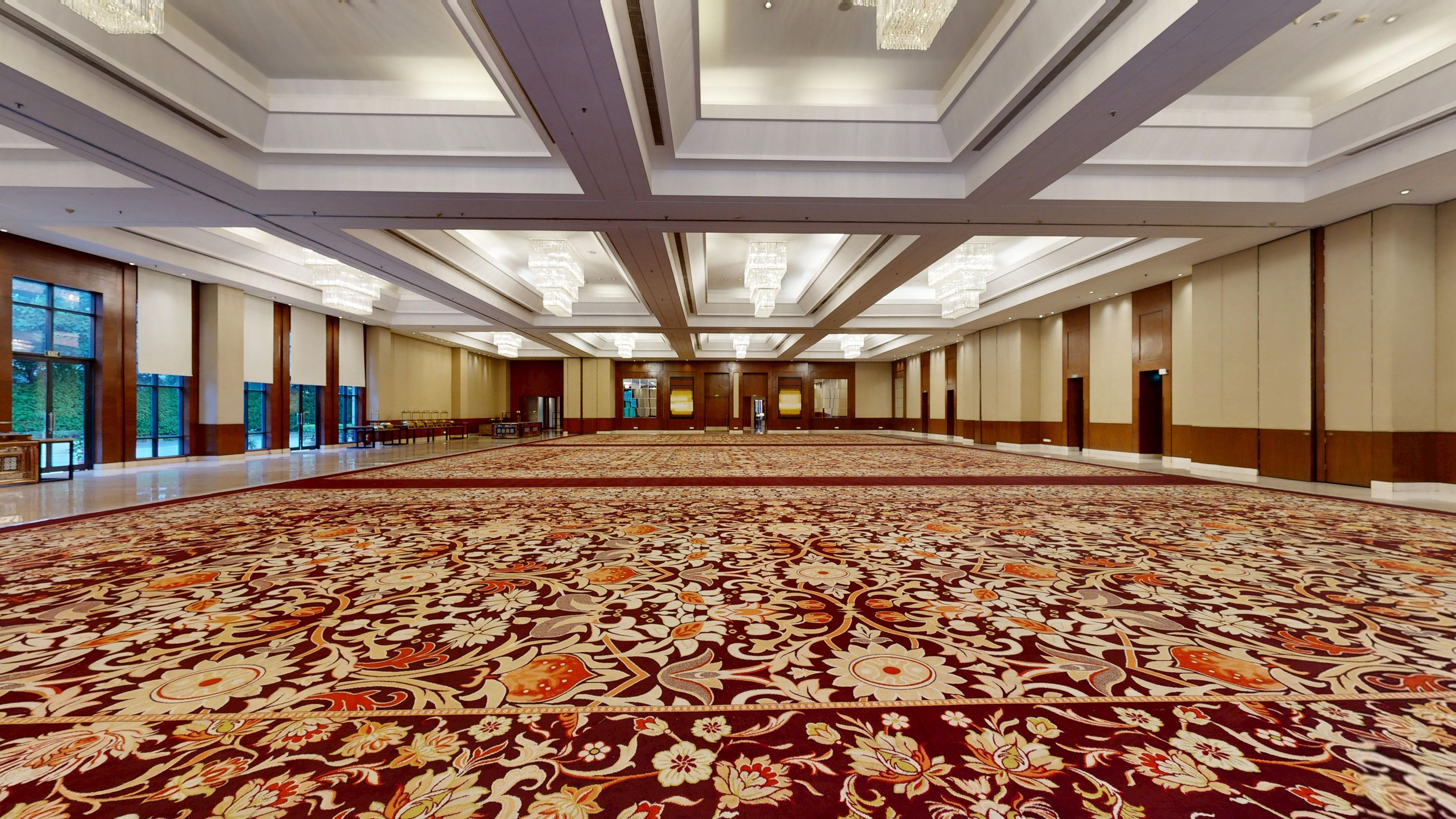 Un vaste hall doté d’un tapis à motifs, de grandes fenêtres et d’un plafond haut orné de lustres.