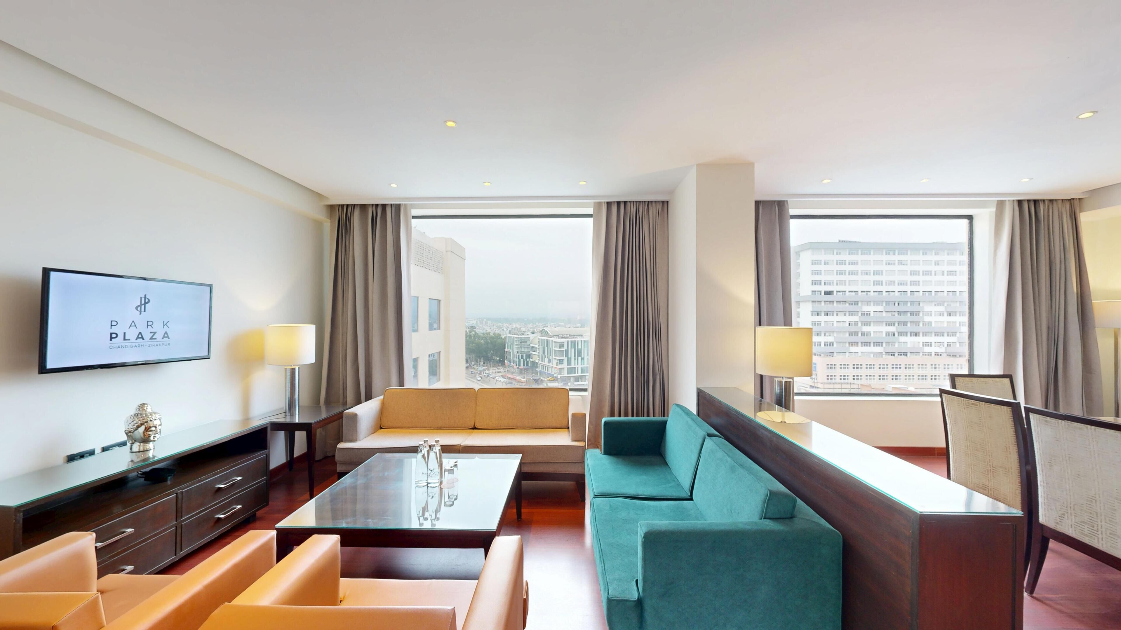 A hotel room with a sofa, a coffee table, a TV, and a city view.