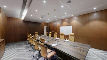 A conference room with a long table, multiple chairs, a whiteboard, and a projector screen.