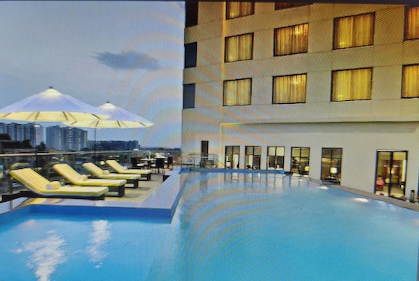Una piscina en la azotea con tumbonas y un edificio con múltiples ventanas.