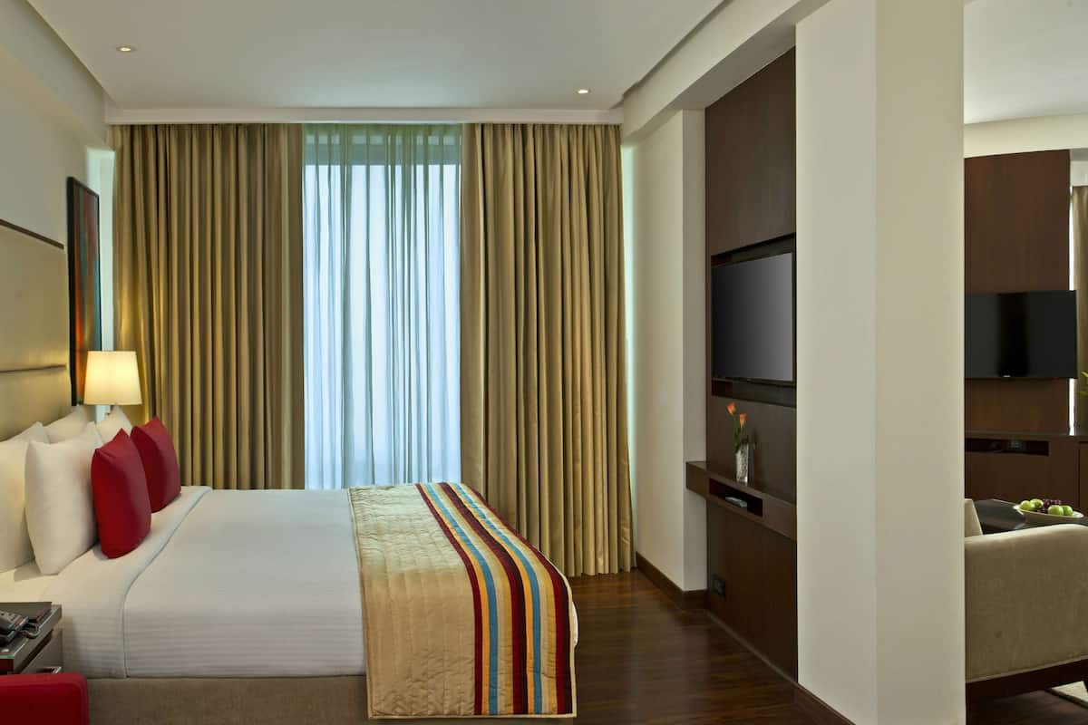 Une chambre d’hôtel avec un grand lit, un bureau avec une lampe, une télévision et un coin repas avec une table et des chaises.