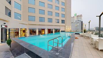 A rooftop pool with a clear view of the cityscape, a hotel building with multiple floors, and a sign for a nearby hotel.