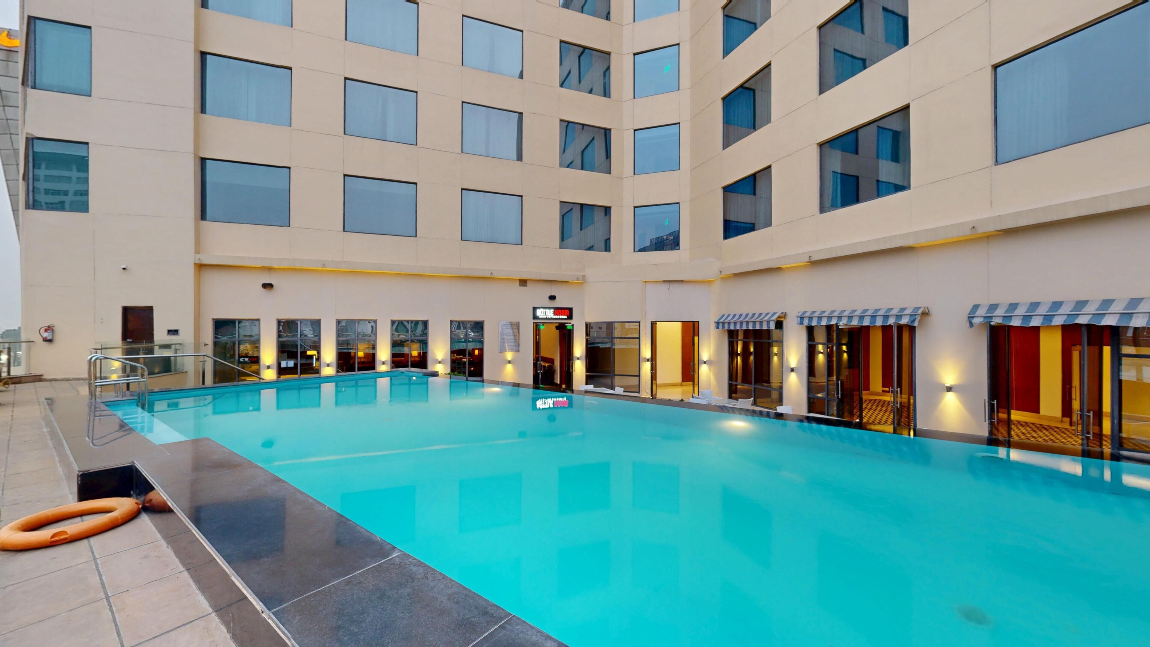 Une vaste piscine intérieure à l’eau d’un bleu limpide, entourée d’un immeuble d’hôtel à plusieurs étages, doté de nombreuses fenêtres et d’un sol carrelé.