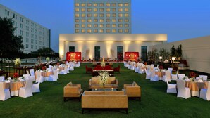 An outdoor event space with tables and chairs, a stage, and a large building in the background.