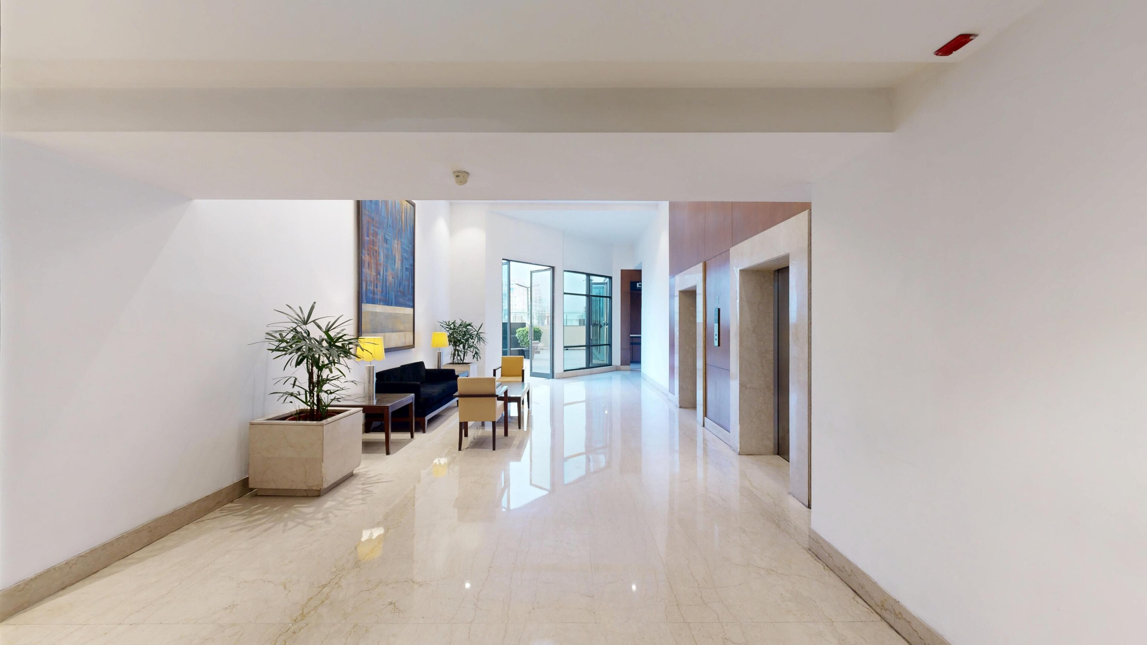 A modern interior with a hallway leading to a dining area, featuring a sofa, chairs, and potted plants.