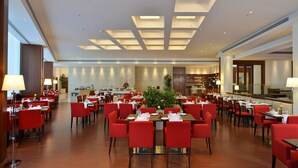 A hotel dining area with red chairs, tables, and a central plant.